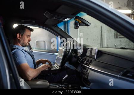 Car mechanic using laptop for diagnostics inside a vehicle Stock Photo