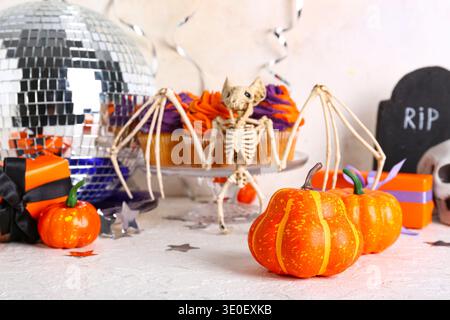 Tasty cupcakes with disco ball, gift boxes, bat skeleton and Halloween decor on white background Stock Photo
