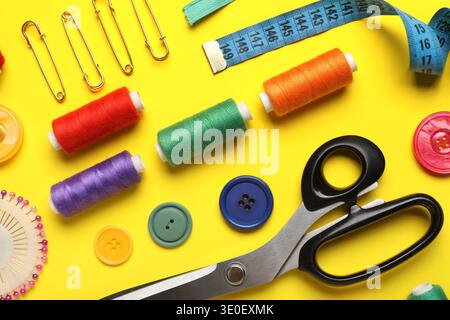 Composition with different thread spools and sewing accessories on yellow background, closeup Stock Photo