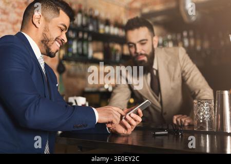 Businessman showing information on phone to barman Stock Photo