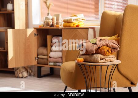 Stack of stylish clothes with autumn decorations on stool near open commode in living room Stock Photo