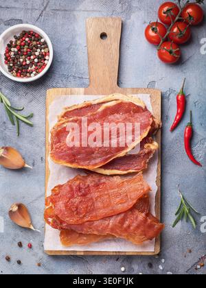 A top view of pieces of smoked pork and chicken on a wooden tray, surrounded by various ingredients and vegetables on the table Stock Photo