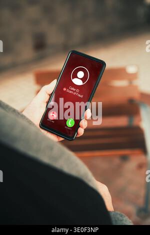 Close up of a person holding a smartphone with an incoming scam of fraud call alert on screen. Stock Photo