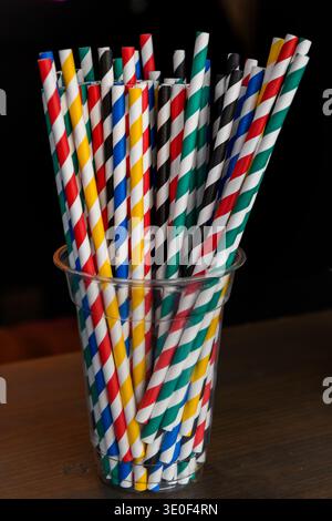 A clear, glass cup holding multi-colored, paper drinking straws with a colorful, spiral design. Stock Photo