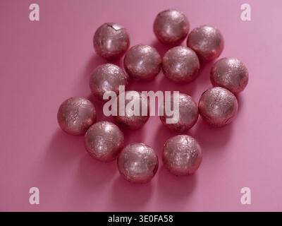 Group of chocolate spheres wrapped in pink foil scattered on a pink background. Stock Photo
