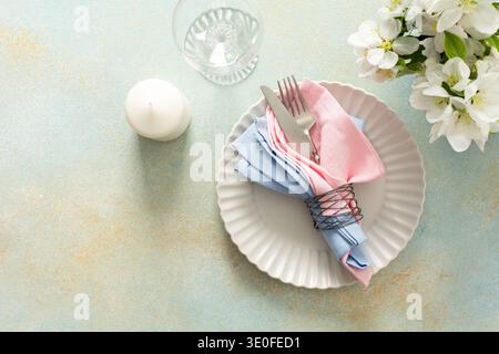A beautiful spring table setting showcases soft pastel napkins neatly arranged on a plate alongside a candle and fresh flowers, creating an inviting dining atmosphere. Stock Photo