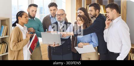 Senior mentor guiding students in collaborative office classroom workshop Stock Photo
