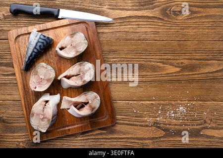 Raw mackerel fish steaks on wooden cutting board with knife and sea salt rustic kitchen background Stock Photo