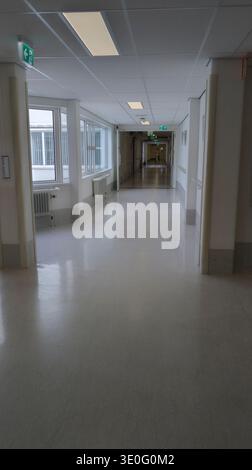 Empty Hospital Corridor With Natural Light, Clean Linoleum Floor and Illuminated Exit Signs Stock Photo