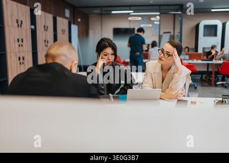 Business meeting in a modern office with three professionals collaborating at a shared table Stock Photo
