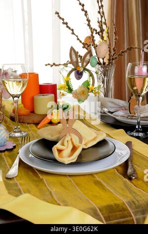 Festive Easter table setting with bunny napkin holder, candles, champagne glasses and spring decorations. Colorful holiday brunch scene with eggs, flo Stock Photo