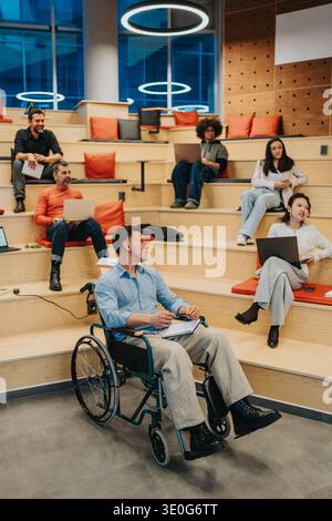 Inclusive team workshop in a modern lecture space with a wheelchair user and laptops collaboration Stock Photo