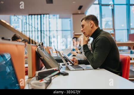 Focused man working on laptop and tablet in a modern library study area Stock Photo