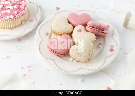 French sweet cookies macarons macaroon with color sprinkles on retro plate on marble table background. Heart shape macarons, cupcake and decor. Stock Photo