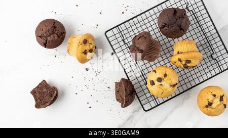 Fresh baked muffins with chocolate chips on baking rack and on white marble table background. Chocolate  cupcake closeup as dessert for coffee break. Stock Photo