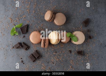 French sweet cocoa cookies macarons macaroons with crumbs, mint and chocolate pieces on dark grey stone background. Macarons in trendy color 2025 Moch Stock Photo