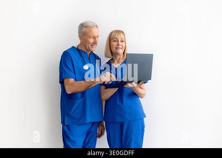 Senior male and female doctors in medical scrubs reviewing information on laptop Stock Photo