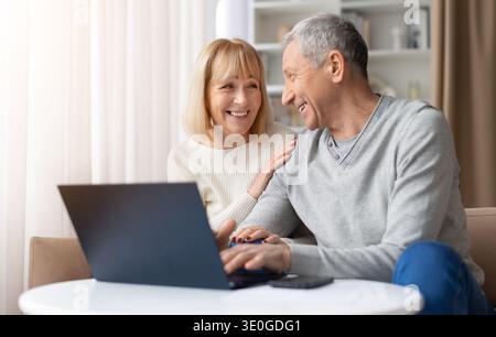 Happy senior couple smiling and using laptop together at home Stock Photo