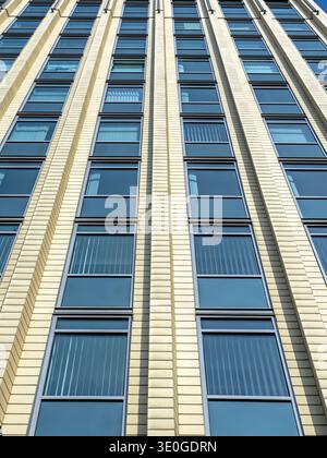 Modern office building facade featuring repeating vertical lines and blue-tinted windows, conveying urban architecture, pattern, symmetry and contempo Stock Photo