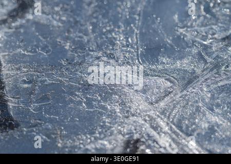 Ice during spring showcases complex fractures with shimmering highlights. Intricate web of cracks and veins arcs across pale blue ice sheet in spring Stock Photo