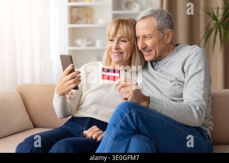 Senior couple using smartphone and credit card for online shopping at home Stock Photo