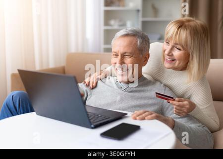 Happy senior couple using laptop while holding credit card at home Stock Photo