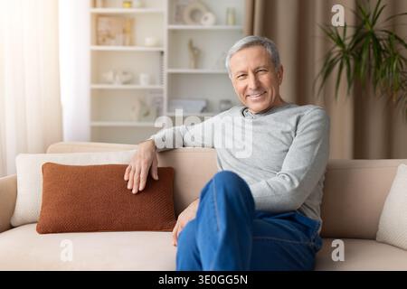 Smiling senior man sitting comfortably on sofa in living room at home Stock Photo