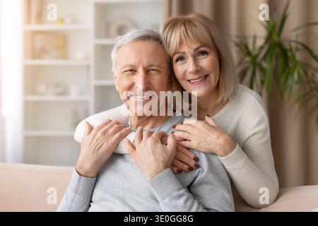 Portrait of smiling senior couple embracing together on sofa at home Stock Photo