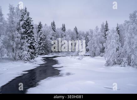 The partially frozen Hepojoki river flowing through the snow covered trees of a pine forest in northern Finland Stock Photo