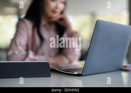 Asian adult woman engages laptop computer with earphones in modern workspace remote work online education business productivity digital tasks Stock Photo