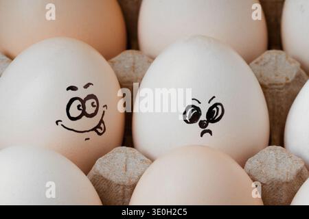 Two white eggs with funny and angry painted faces in a cardboard carton. A creative concept showing emotions, personality, and humor in everyday objec Stock Photo