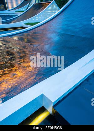 A close-up view of fluid water flowing over architectural curves with warm golden lighting. The image conveys motion, abstraction, and modern landscap Stock Photo