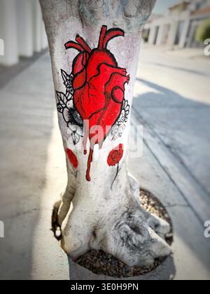 Close up of a painted anatomical heart with dripping red color and flowers on a tree trunk outdoors Stock Photo