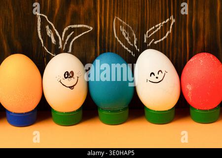 Funny Easter eggs with painted faces and chalk bunny ears on wooden background. Stock Photo