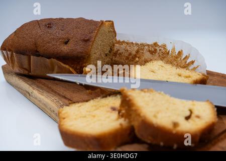 Sweet pound cake or plum cake loaf, partially sliced with a knife on a rustic wooden cutting board, ready for eating Stock Photo