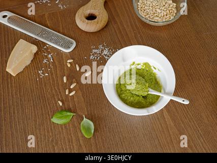 Fresh homemade basil pesto sauce in white bowl on wooden table. Top view of traditional green pesto Genovese inside ceramic bowl with spoon surrounded Stock Photo