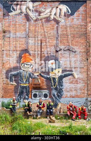 Workmen taking a break sitting in front of the now demolished Hip Hop Marionettes mural by artist Rogue One, George Street, Glasgow, Scotland, UK Stock Photo