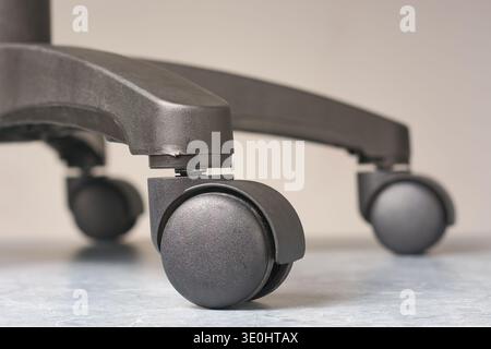 black office chair plastic casters, base and dual wheels on grey textured floor, close up in low angle with copy space, office furniture and mobility Stock Photo