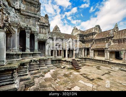 Visitors explore the ancient Angkor Wat temple complex in Cambodia under a clear blue sky. The structure holds historical importance. Stock Photo