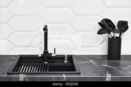 Contemporary kitchen interior with matte black sink and faucet on marble countertop. Minimalist home design with hexagon tile backsplash. Stock Photo
