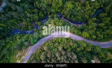 Aerial view of a winding road following the edge of a lush green lake ...