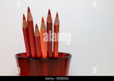 Set of red and orange colored pencils arranged in a translucent glass holder with clean copy space, ideal for education, creativity, and art concepts. Stock Photo