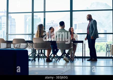 Mature businessman talking with diverse team sitting at table in office with city view during daytime Stock Photo