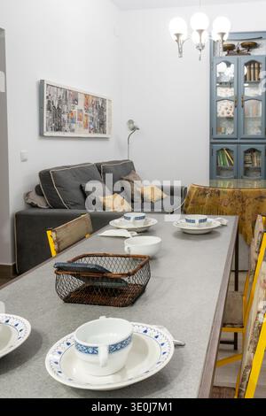 Dining table set with white and blue cups, saucers, and bowls in a modern living room interior featuring a sofa Stock Photo