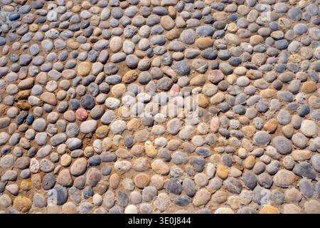 A top-down view of a cobblestone path made of smooth colorful river stones embedded in sand. This rustic stone surface represents traditional masonry, Stock Photo