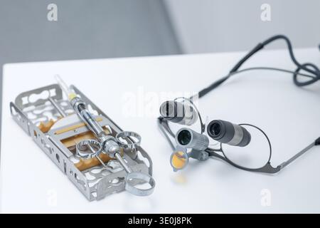 Closeup of dental loupes, surgical syringe and metal tray instruments on white surface. Concept of endodontic treatment, anesthesia and precision dent Stock Photo