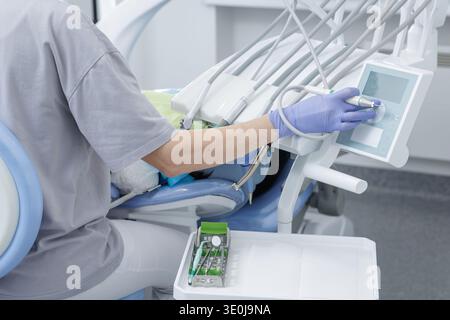 Dentist adjusting dental unit while performing professional teeth cleaning in modern clinic. Advanced equipment and oral healthcare treatment environm Stock Photo