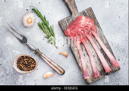 Uncooked lamb ribs and cutlets with herbs and spices on wooden board stone background top view butcher preparation. Stock Photo