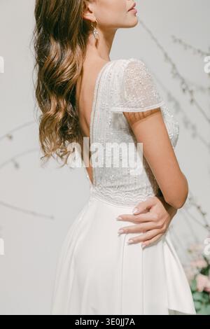 A woman stands in a studio showing a bridal dress design. Her hairstyle flows down her back. The setting features soft lighting and background details Stock Photo