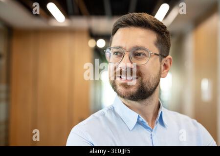 Professional businessman wearing glasses with a beard smiling, posing confidently in an indoor office environment, representing success, achievement, and corporate leadership Stock Photo